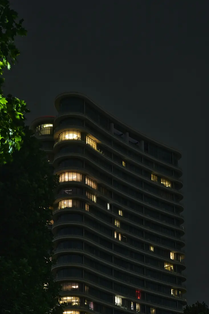 Ağacın yanında kavisli cepheli, pencereleri yanan apartman