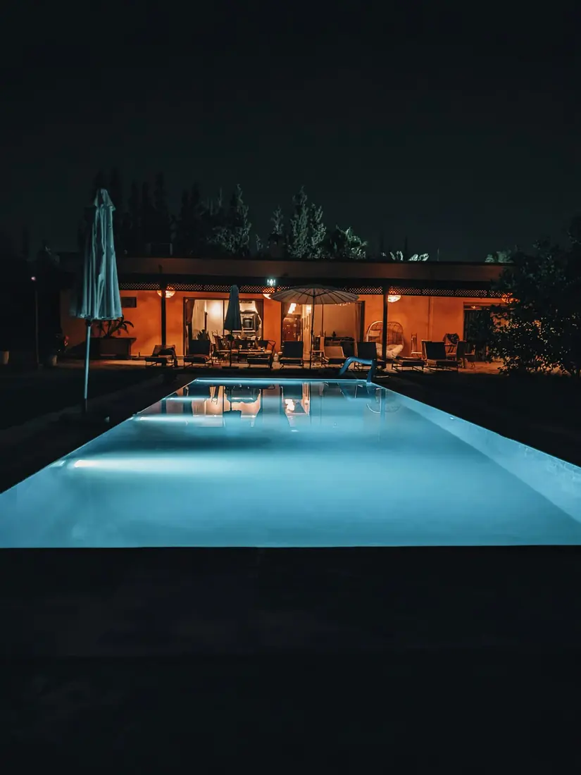 Gece aydınlatılmış havuz ve arkasında cam cepheli ev